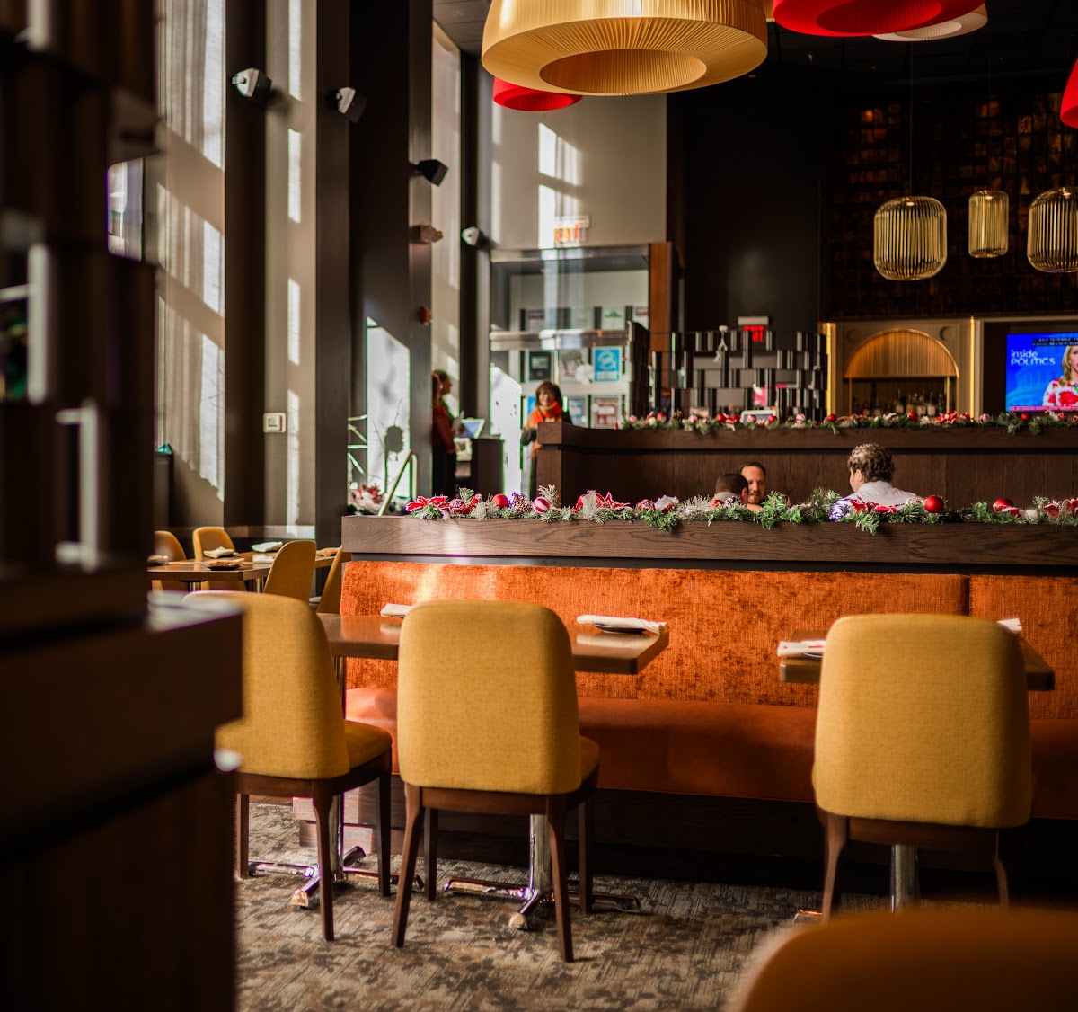 The warm dining room at Douzo with mustard chairs, an orange velvet banquette, and gold pendant lighting